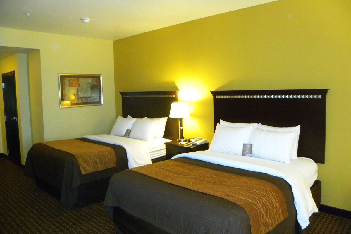 A hotel room with two beds, a nightstand with a lamp, and a painting on the wall.