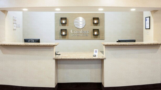A reception area with a sign reading "Comfort Inn & Suites," two reception desks, a small display case, and a framed picture on the wall. - Comfort Inn & Suites Regional Medical Center (Abilene)