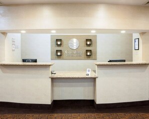 A reception area with a sign reading "Comfort Inn & Suites," two reception desks, a small display case, and a framed picture on the wall. - Comfort Inn & Suites Regional Medical Center (Abilene)