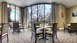Un espace de restauration d’hôtel doté de grandes fenêtres, de nombreuses tables et de chaises.