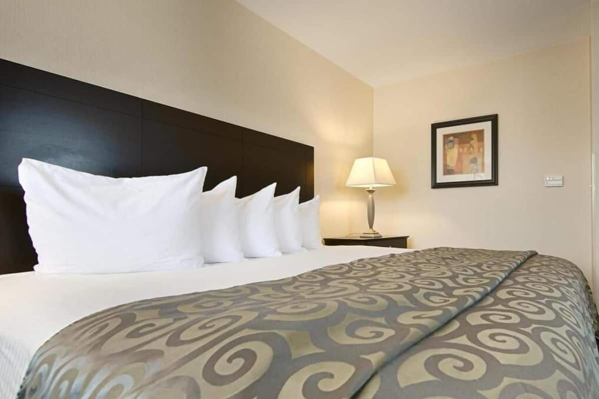 Een hotelkamer met een bed, een nachtkastje met een lamp, en een lijst met een afbeelding aan de muur.