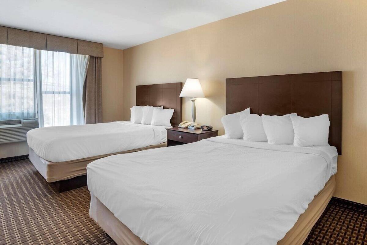 Een hotelkamer met twee bedden, een nachtkastje met een lamp en een raam met gordijnen.