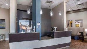 Un comptoir d’accueil avec une cloison en verre, un mur d’accent bleu et des luminaires suspendus.