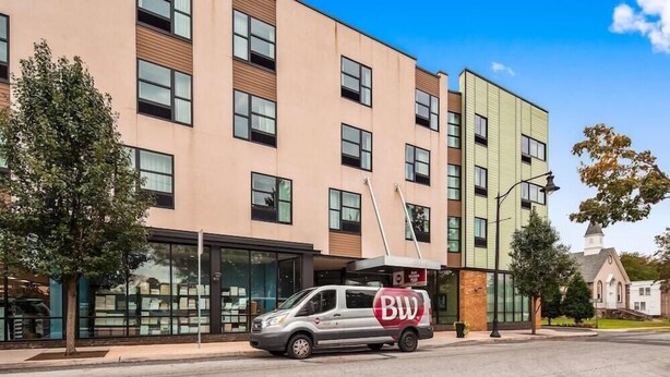 Un immeuble à plusieurs étages, doté d’une architecture moderne, avec une façade combinant verre et briques, et un fourgon stationné devant, arborant le logo « BW ».