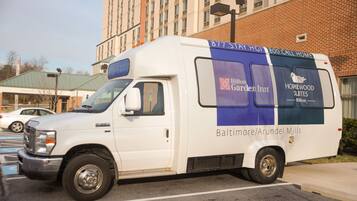 A white van with "HILTON GARDEN INN" branding and "HOMEWOOD SUITES" text, parked in a lot with a brick building in the background.