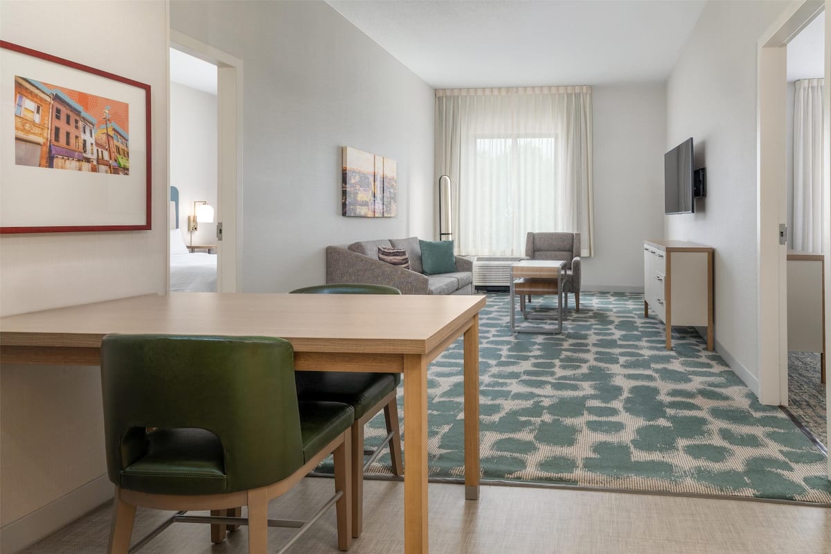 Une chambre d’hôtel moderne avec un coin repas, un canapé, une télévision et des œuvres d’art accrochées aux murs.