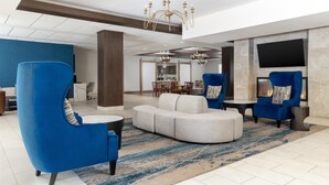 A modern lobby with blue armchairs, a white sofa, and a chandelier.