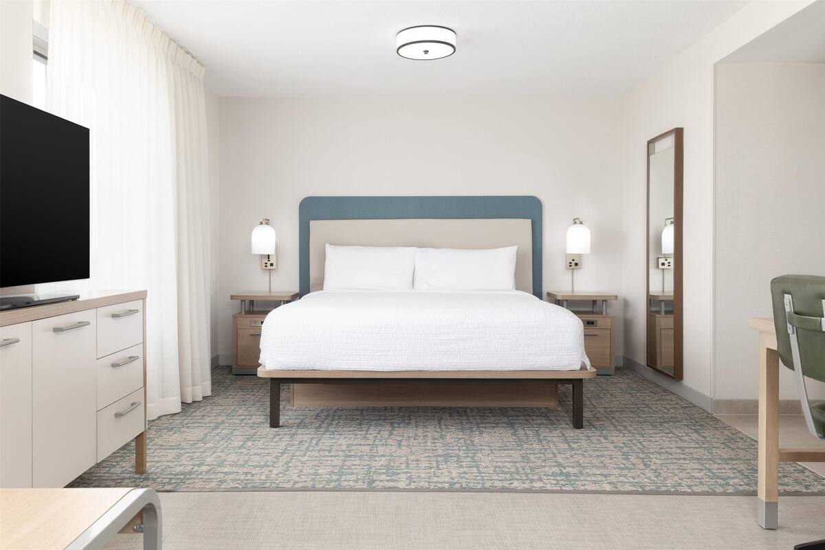Une chambre d’hôtel comprenant un lit, des tables de chevet, une télévision, un miroir et un bureau.