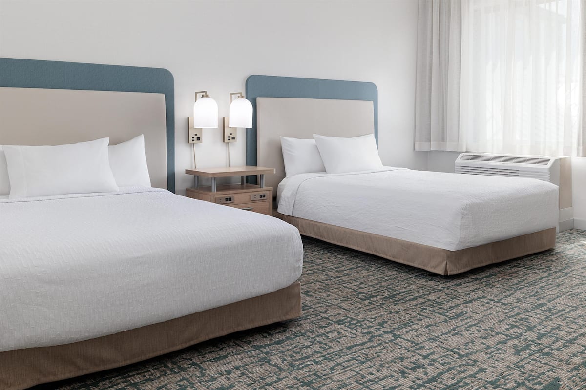 Une chambre d’hôtel avec deux lits, une table de chevet avec des lampes et une fenêtre avec des rideaux.