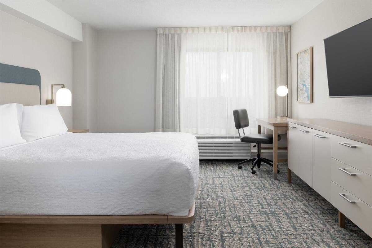 Une chambre d’hôtel équipée d’un lit, d’un bureau, d’une chaise et d’un téléviseur à écran plat fixé au mur.