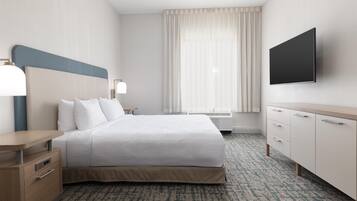 Una habitación de hotel con cama, mesitas de noche, televisión, escritorio y ventana con cortinas.