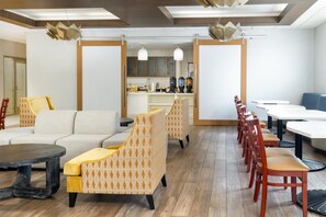 A modern interior with a sofa, patterned armchairs, a dining area with chairs, and a kitchen in the background.
