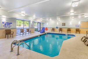 Piscina interior con señalización de seguridad clara, sillas alrededor y vistas al exterior.