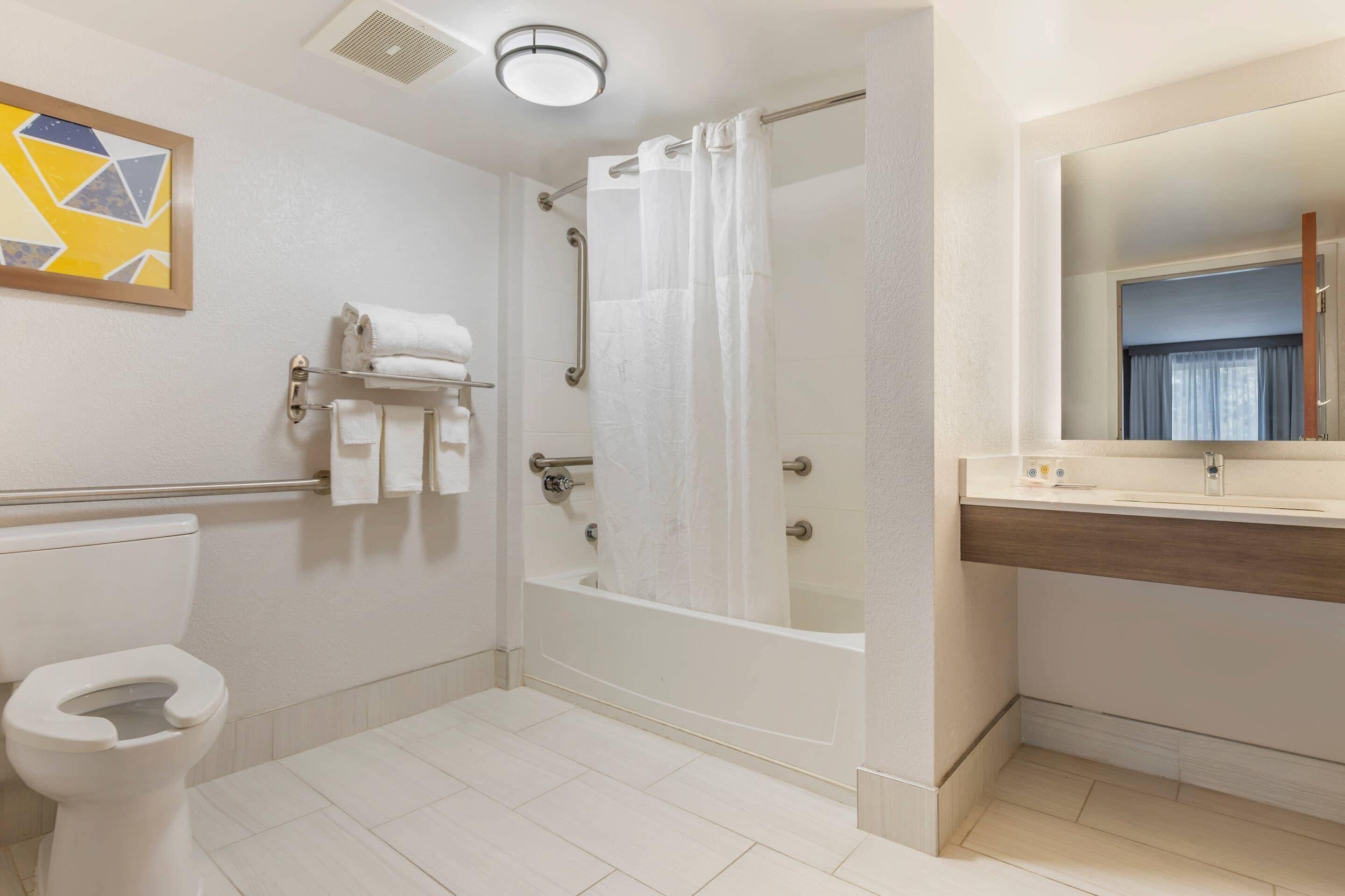Ein modernes Badezimmer mit Toilette, einer Badewanne mit Duschvorhang, einem Waschtisch mit Spiegel und einem Handtuchhalter mit Handtüchern.