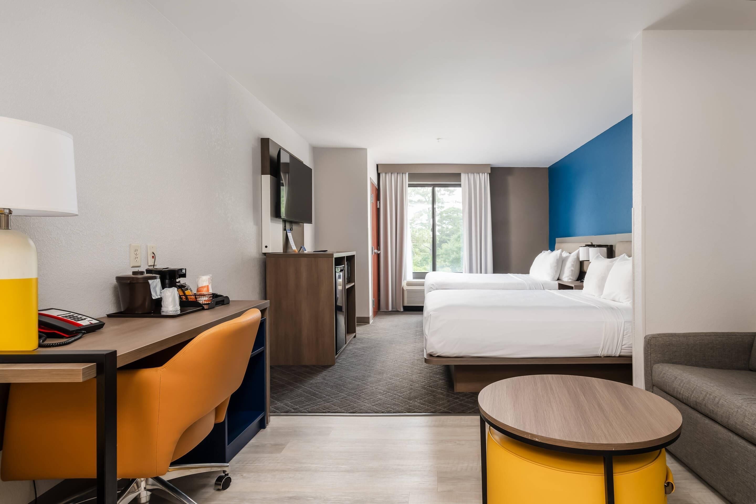 Une chambre d’hôtel avec un lit, un bureau doté d’une lampe, une télévision et une petite table ronde.