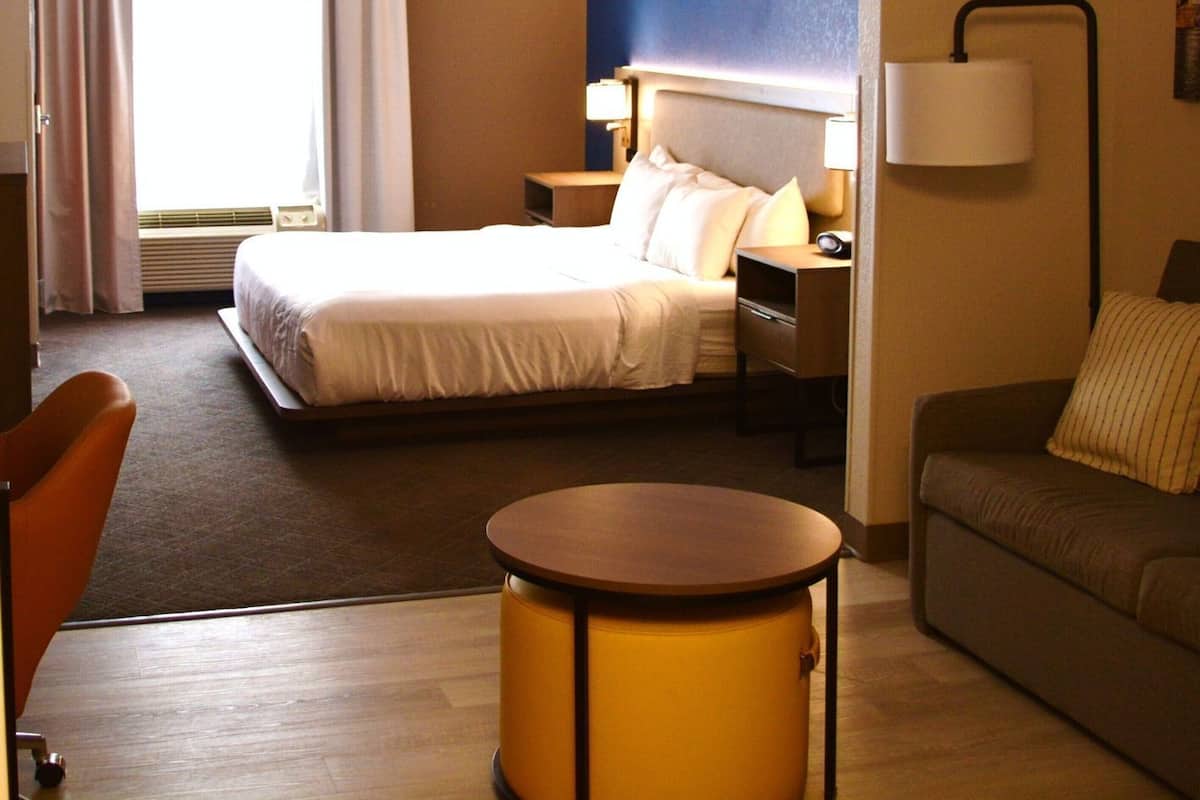 Hotellihuone, jossa on sänky, työpöytä, tuoli, sohva ja lamppu.