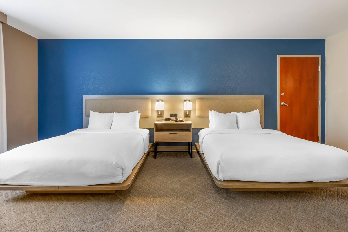 A hotel room with two beds, a nightstand, and a door.