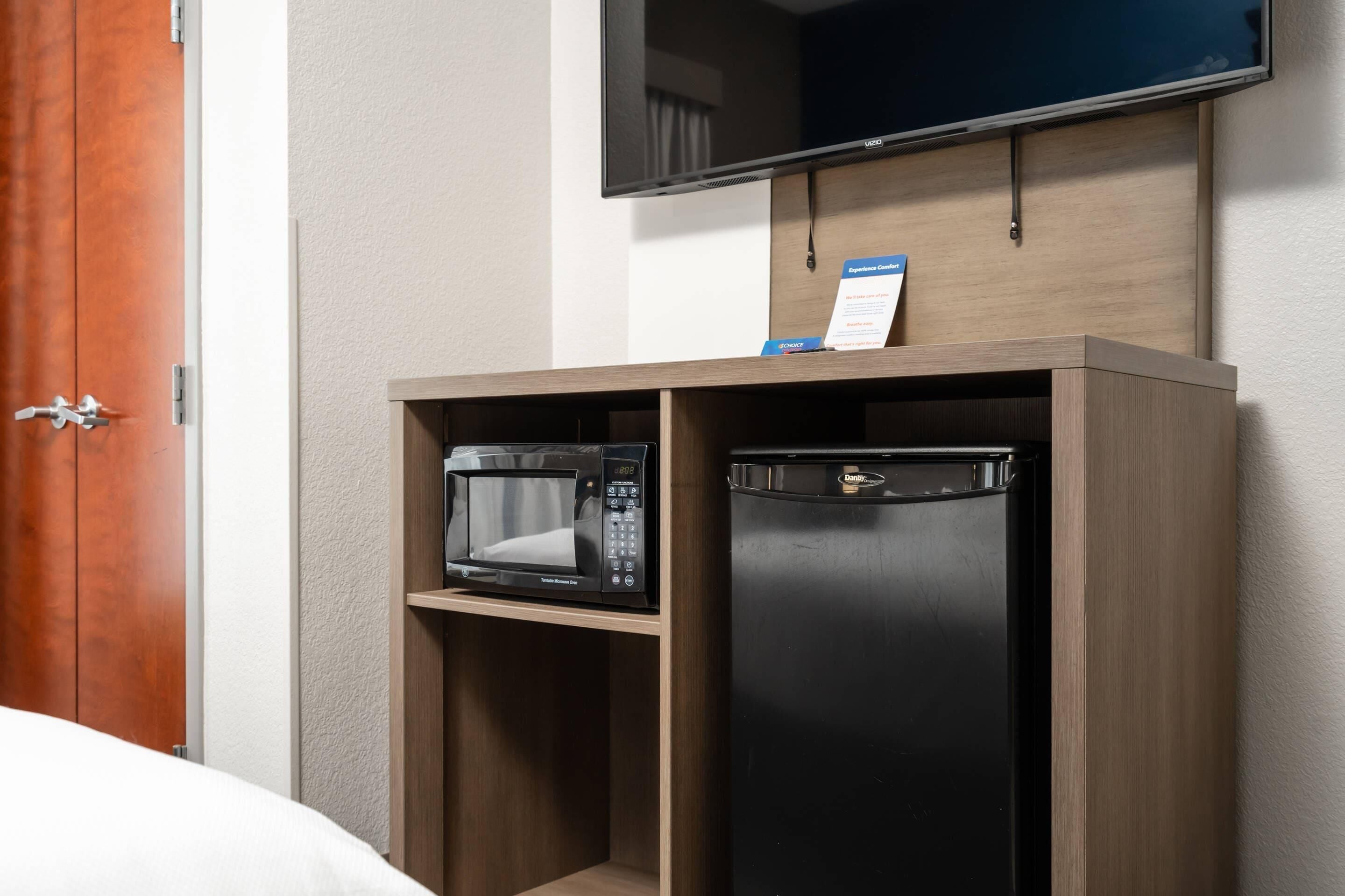 A hotel room with a wooden cabinet containing a microwave and a refrigerator.