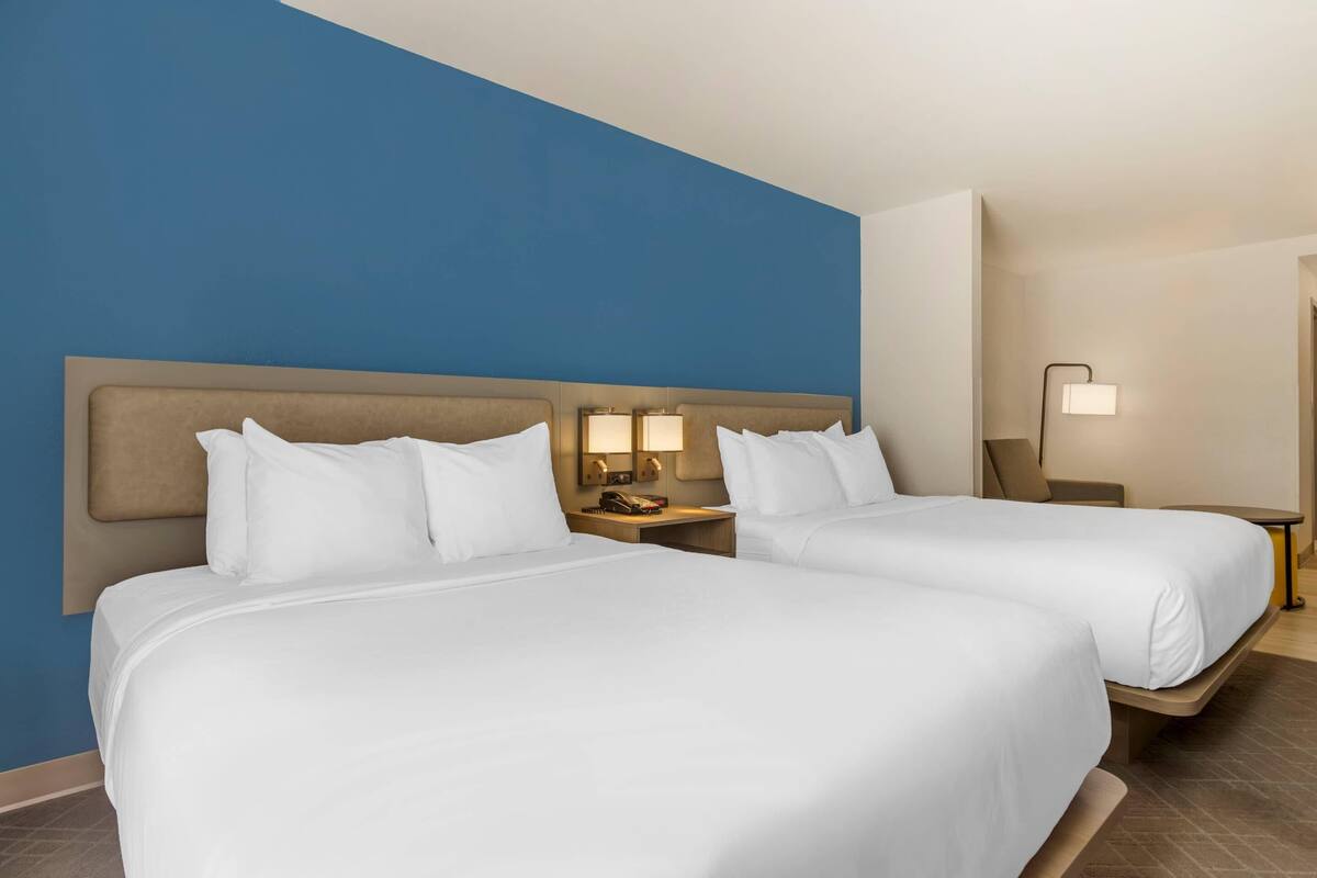 Une chambre d’hôtel avec deux lits, un mur d’accent bleu, une table de chevet avec une lampe et une petite table de nuit avec un téléphone.