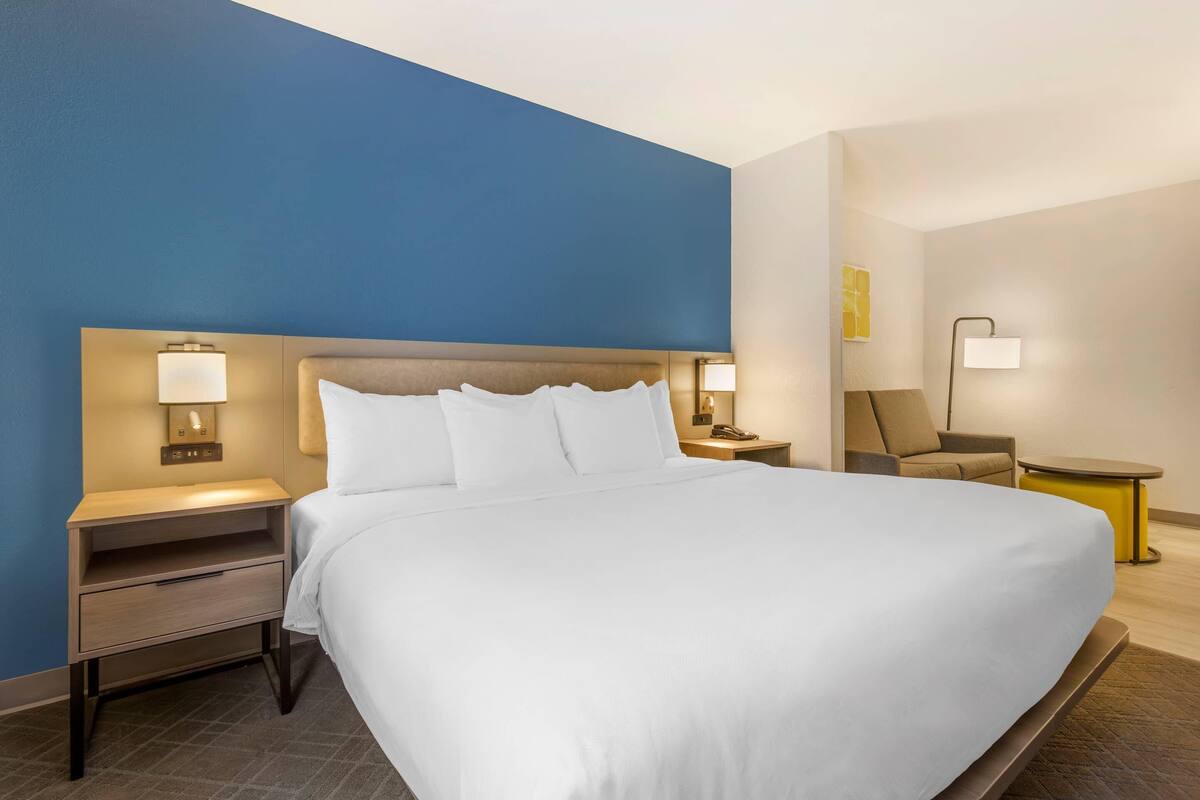 Une chambre d’hôtel avec un grand lit, une table de chevet avec une lampe, une chaise et une petite table.