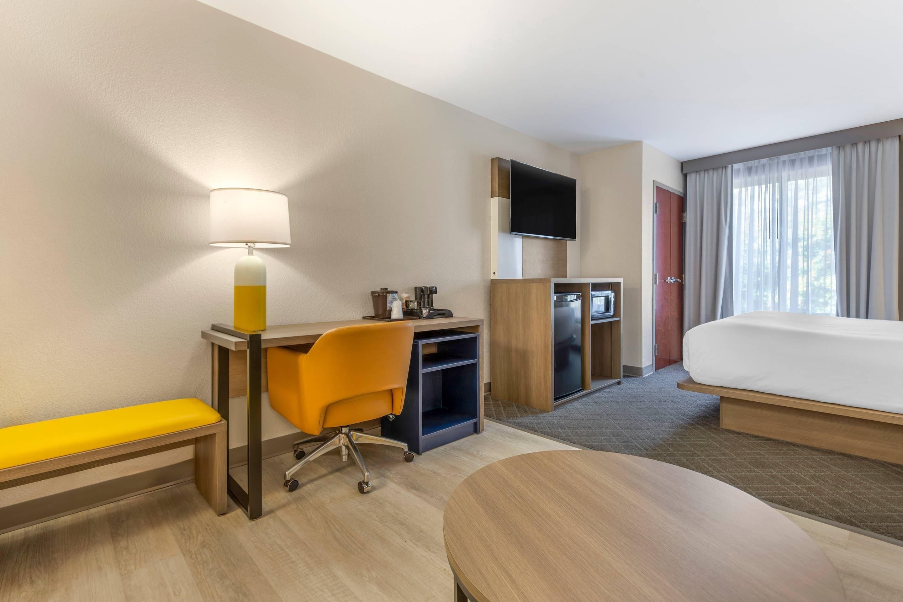 Habitación de hotel con cama, escritorio con silla, televisor y ventana con cortinas.