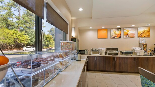 Un espace dédié au petit-déjeuner, avec un comptoir, des présentoirs remplis de pâtisseries et une vue sur les arbres à l’extérieur.
