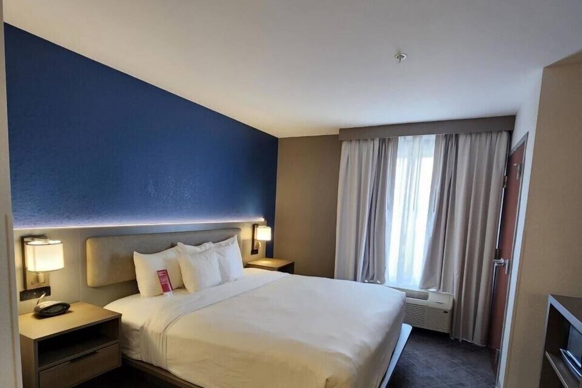Une chambre d’hôtel avec un grand lit, une table de chevet avec une lampe, une fenêtre avec des rideaux et un téléviseur.