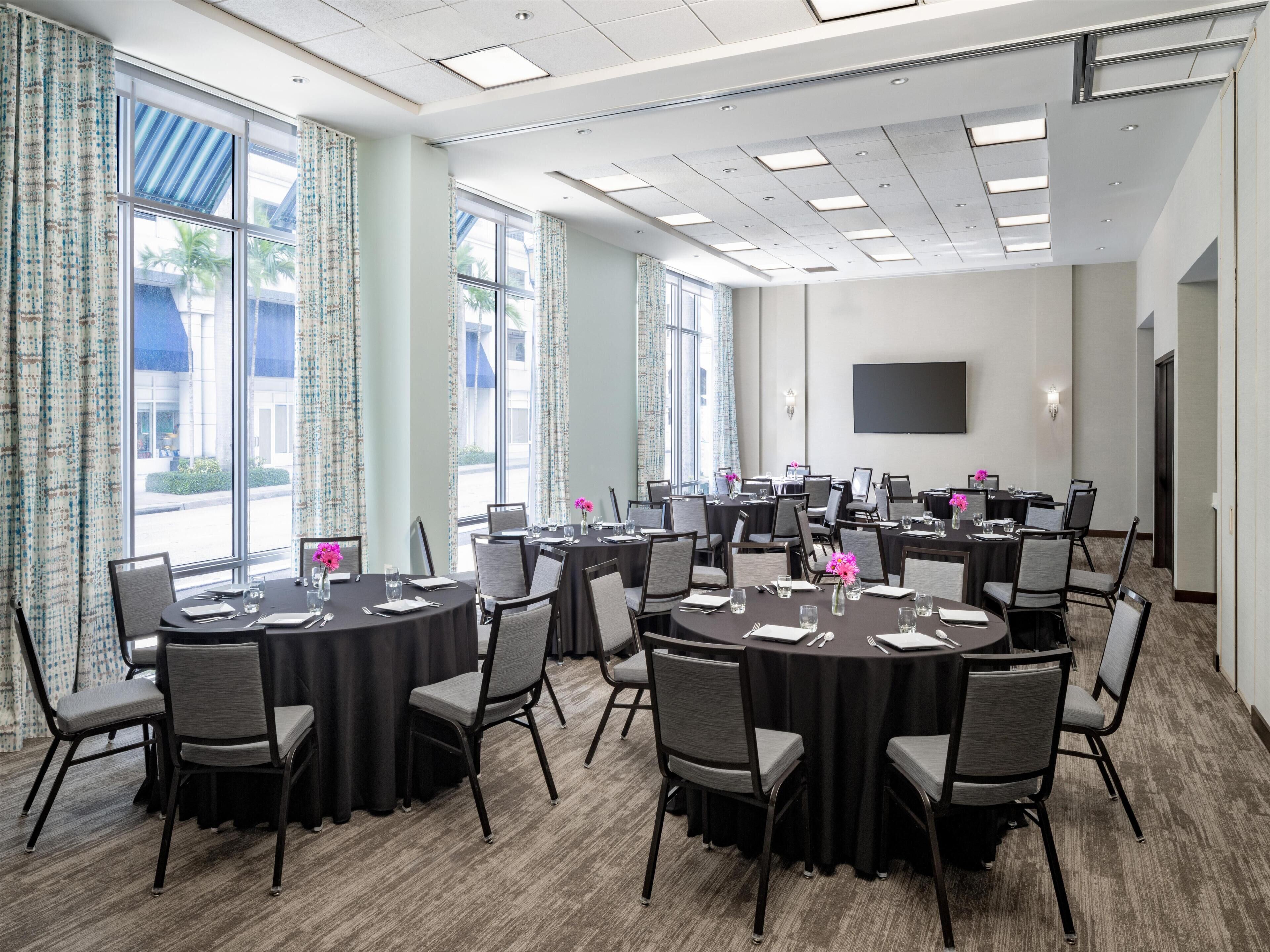 Une salle de conférence équipée de tables rondes, de chaises et d’un grand écran.
