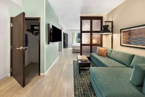 A modern living room with a sofa, a TV, and a large window. - Hyatt Place West Palm Beach/Downtown (West Palm Beach)