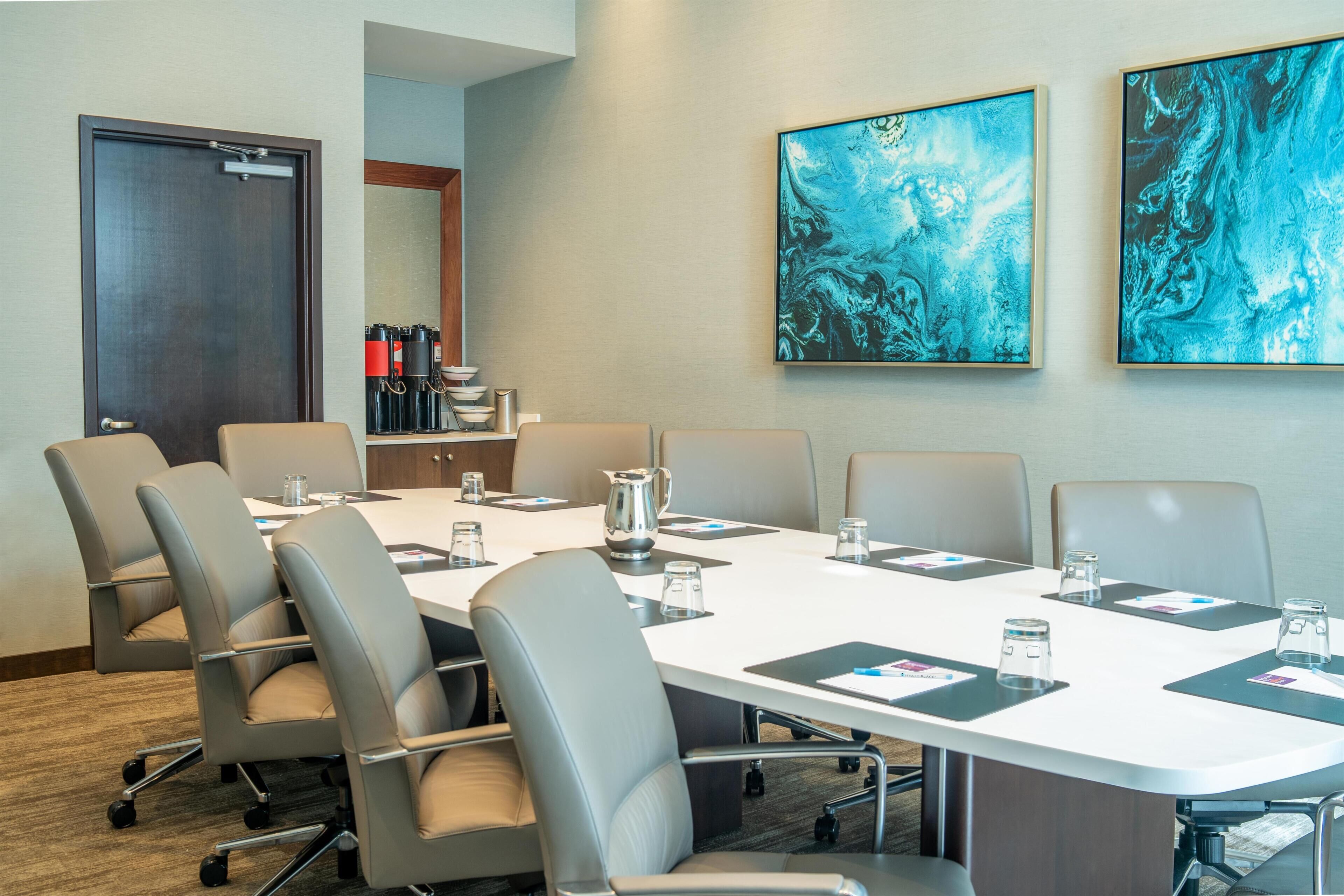 A conference room with a long table, six chairs, and two abstract paintings on the wall.