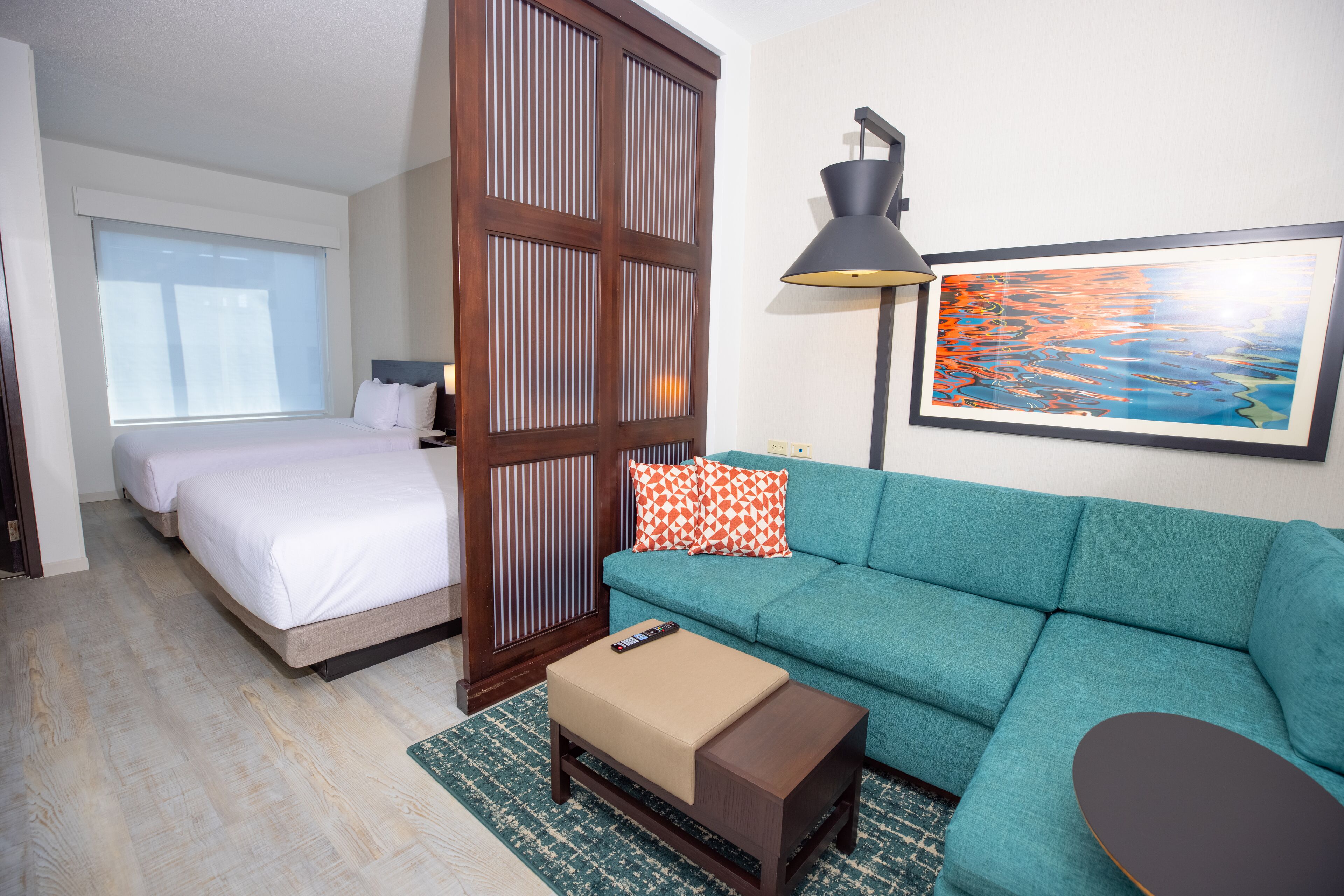 A hotel room with a bed, a sofa, a small table, a lamp, and a painting on the wall.