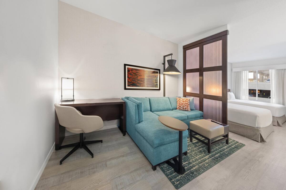 A modern living room with a sofa, a desk, a chair, a lamp, and a window.