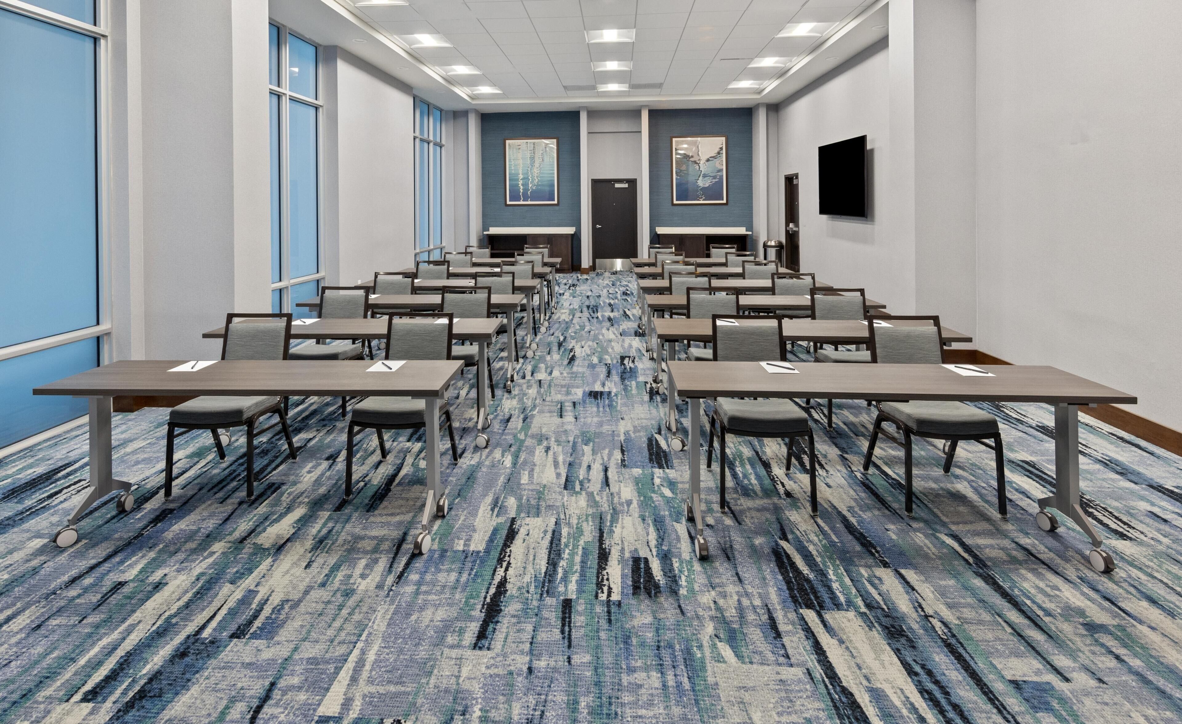 Une salle de conférence avec des rangées de tables et de chaises, une moquette à motifs et une porte au fond.