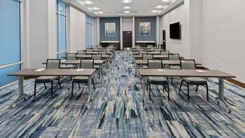 Une salle de conférence avec des rangées de tables et de chaises, une moquette à motifs et une porte au fond.