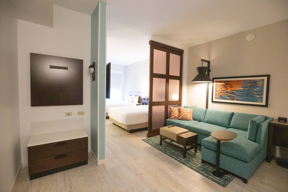 A hotel room with a bed, a sofa, a small table, a desk, a chair, a TV, a painting, and a wardrobe.