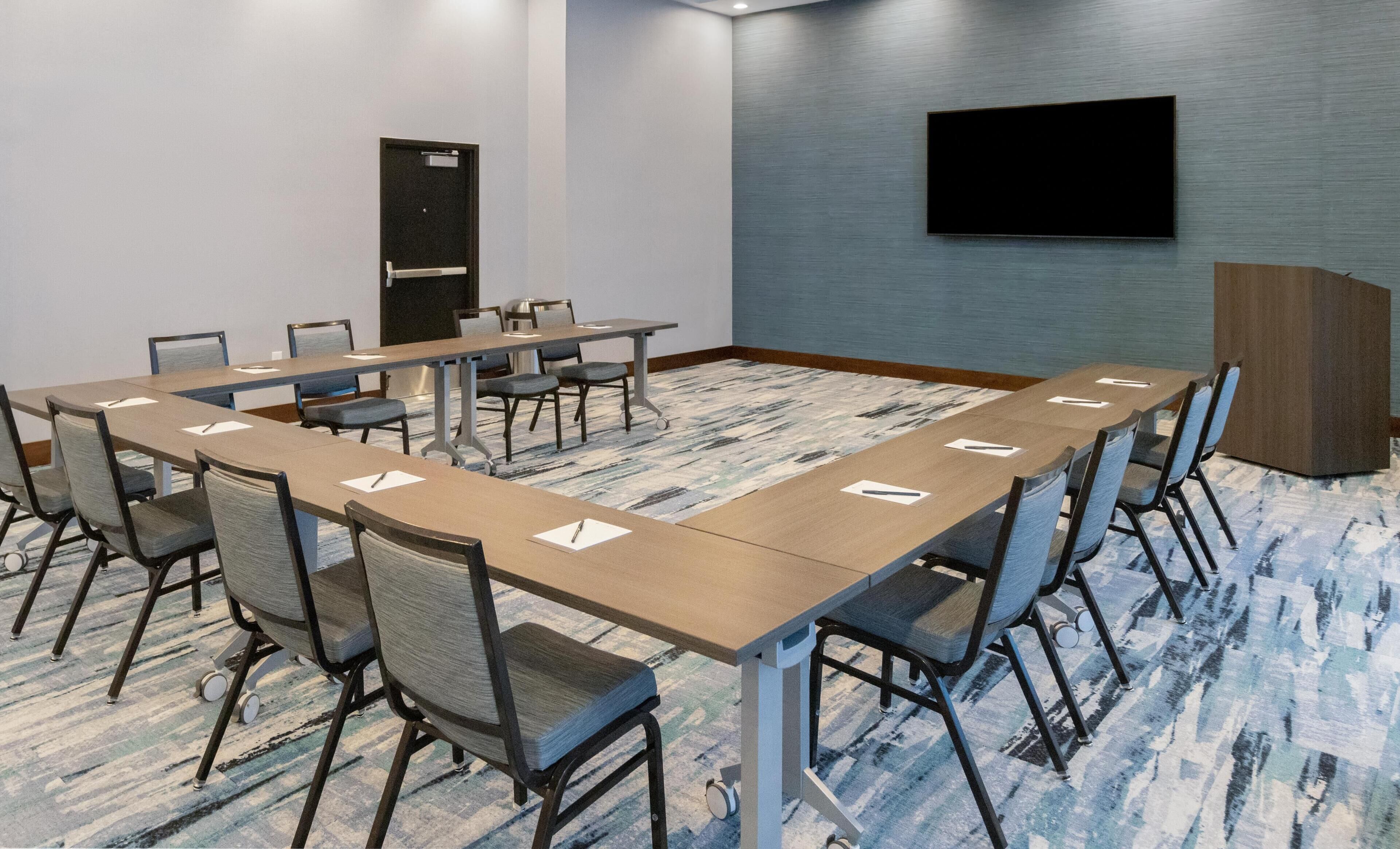 Un salón de conferencias con una larga mesa, sillas, un televisor y una puerta.