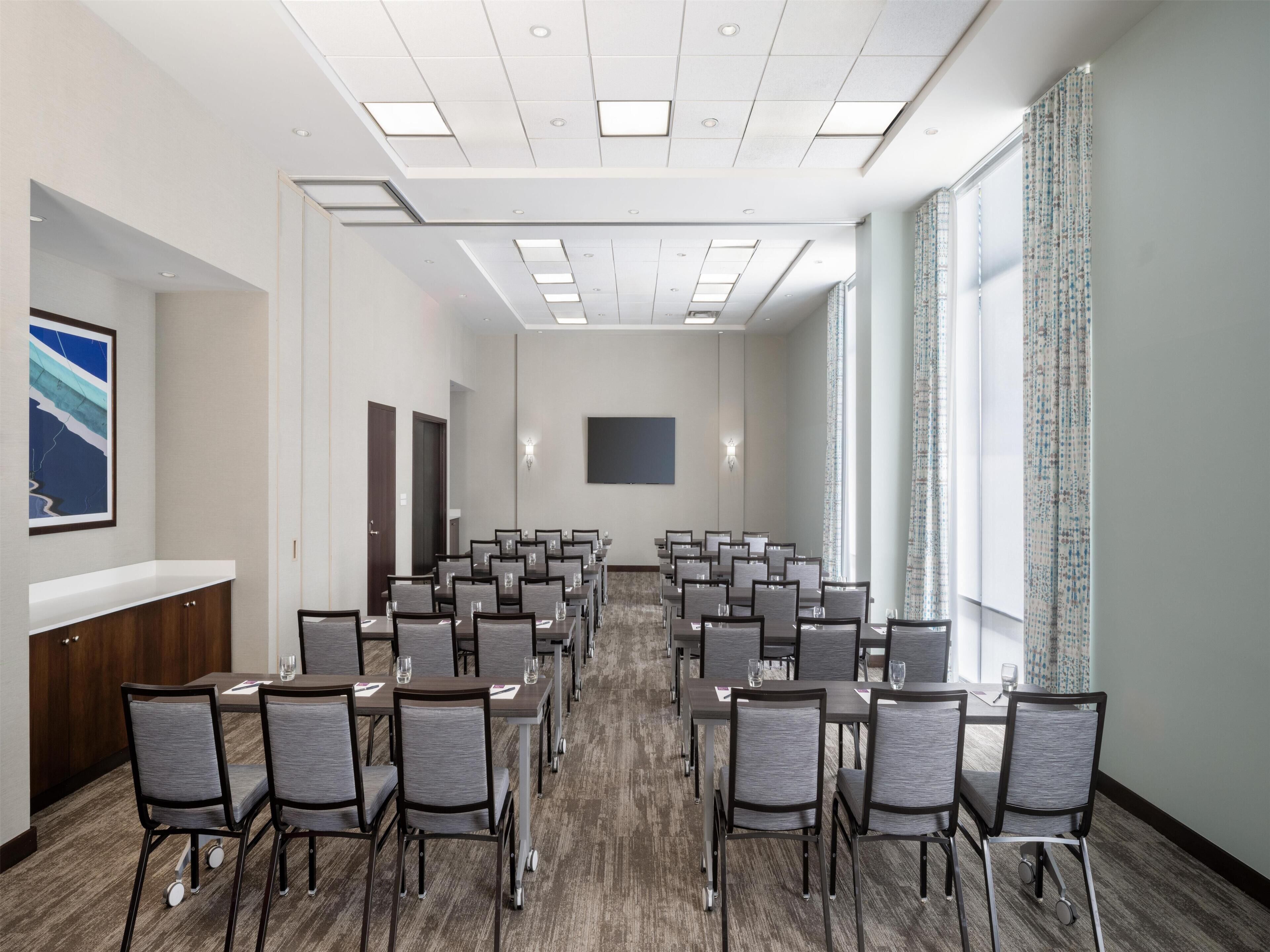 A conference room with rows of chairs, a large flat-screen TV, and a window with curtains.