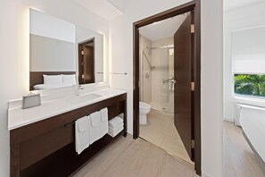 A modern bathroom with a large mirror, white sink, dark wooden vanity, and a glass shower door. - Hyatt Place West Palm Beach/Downtown (West Palm Beach)