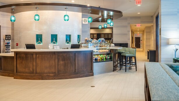 A modern hotel lobby with a curved reception desk, a Starbucks sign, and a bar area. - Hyatt Place West Palm Beach/Downtown (West Palm Beach)