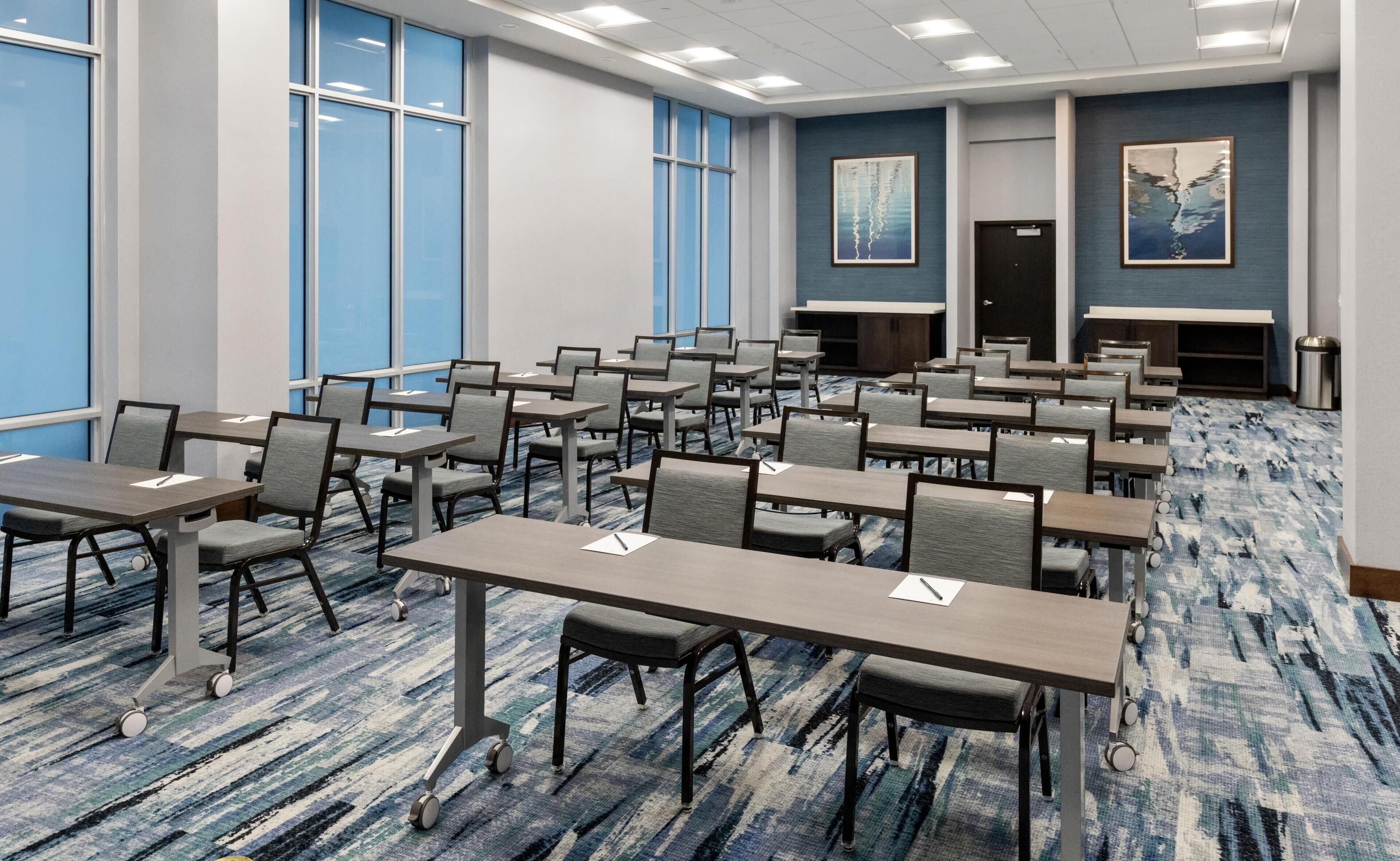 A conference room with rows of tables and chairs, large windows, and artwork on the walls.
