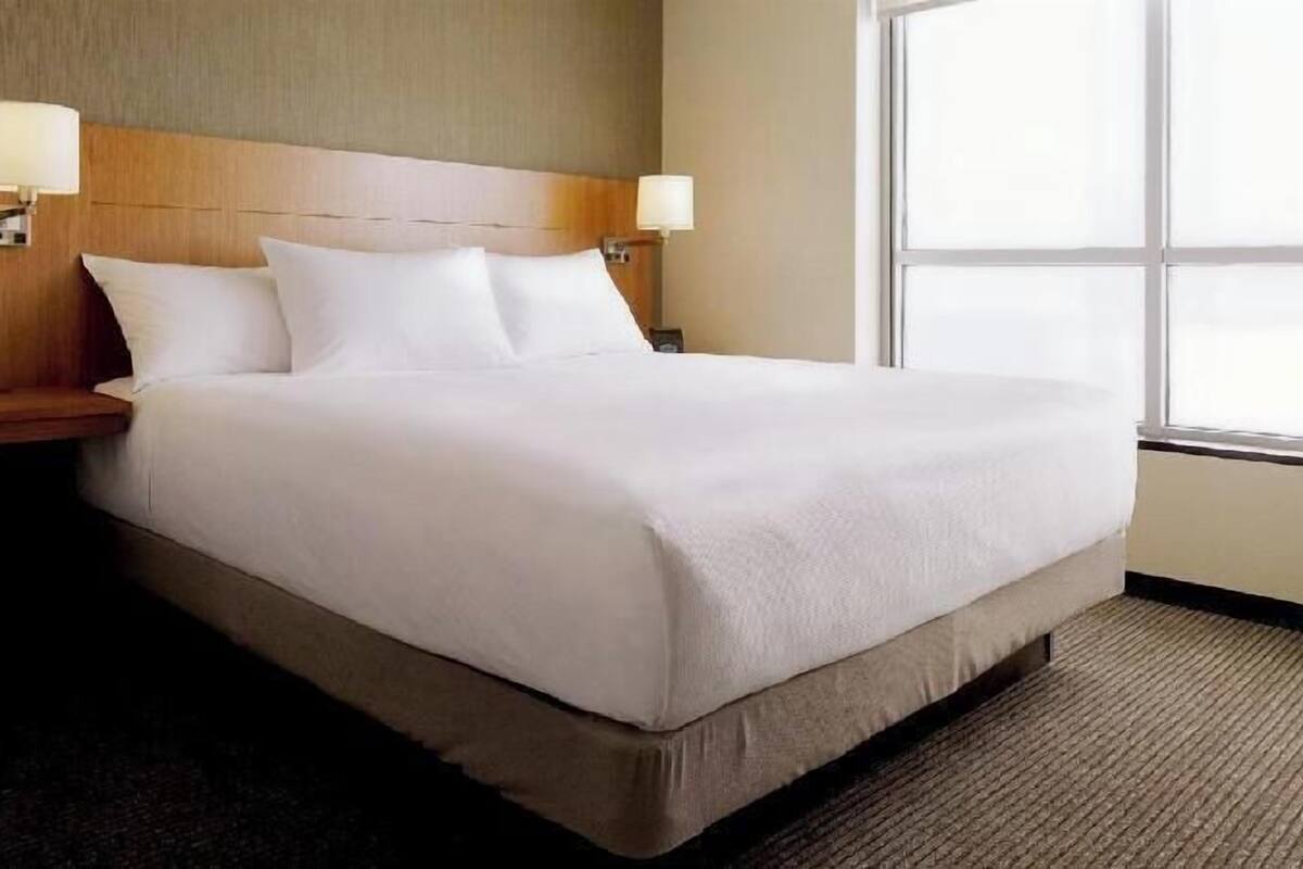 A hotel room with a large bed, two bedside lamps, a wooden headboard, and a large window.