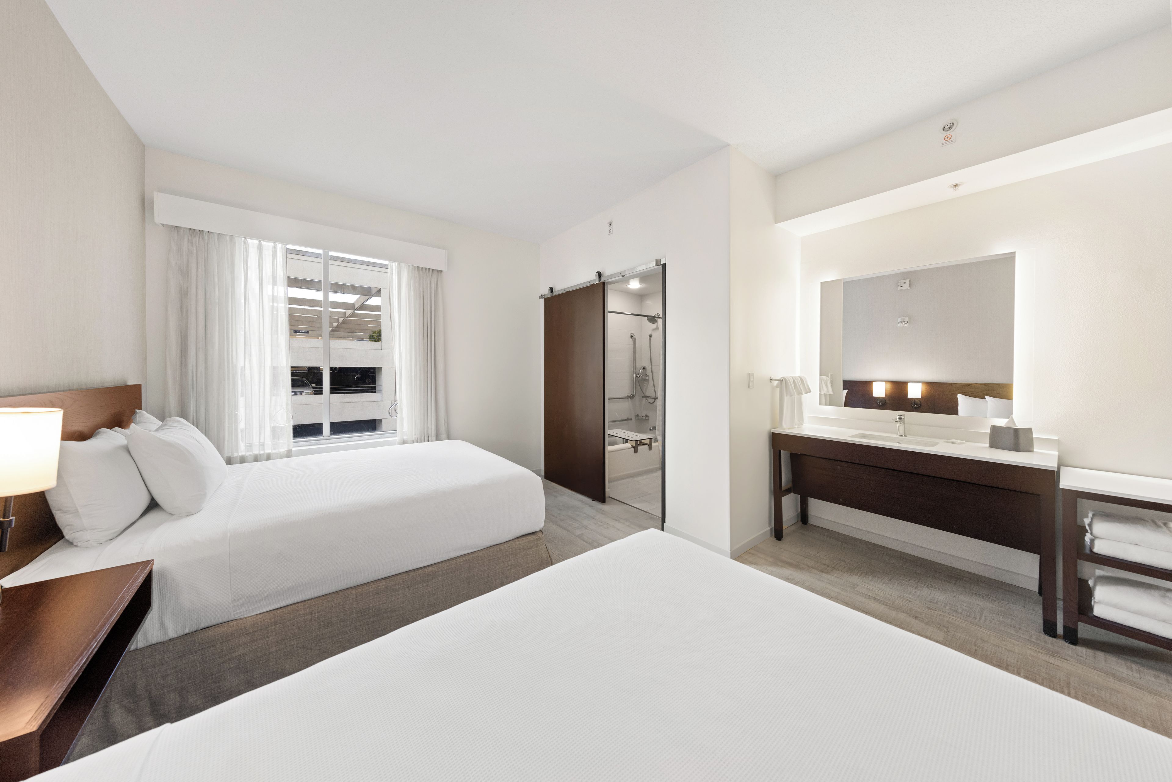 A hotel room with two beds, a bathroom, and a large mirror.