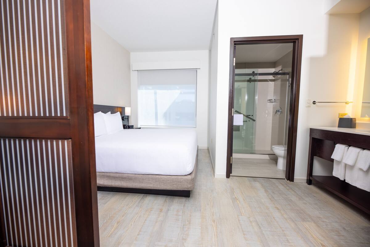 A hotel room with a bed, a bathroom with a shower, and a vanity with a towel rack.