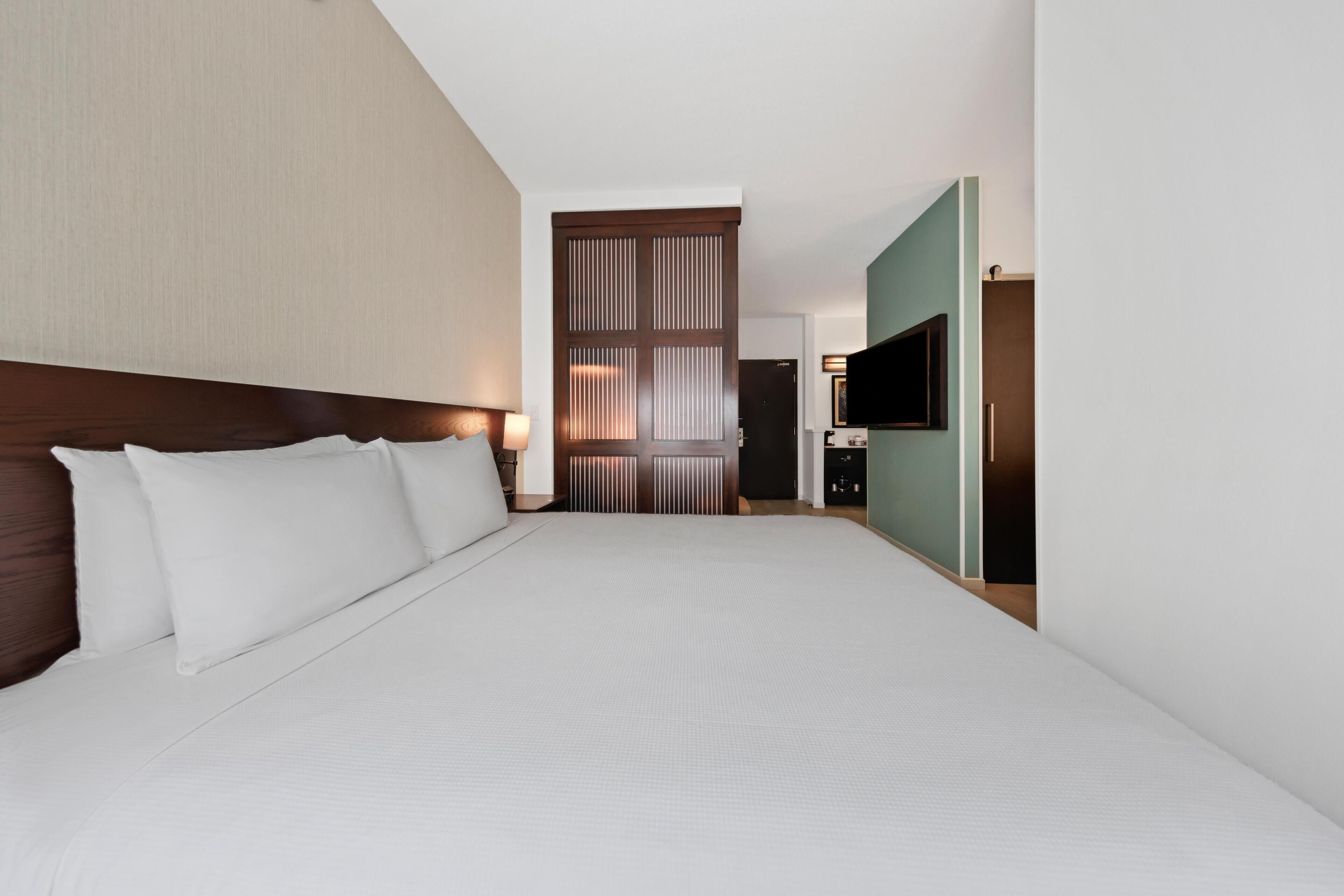 A hotel room with a large bed, a TV, and a sliding door leading to a bathroom.