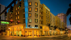 A multi-story hotel with a prominent 'HYATT PLACE' sign, a curved facade, and a street view with traffic lights and palm trees. - Hyatt Place West Palm Beach/Downtown (West Palm Beach)