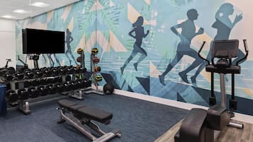 Une salle de sport équipée de matériel d’exercice, d’un téléviseur fixé au mur et ornée d’une fresque murale à motifs.