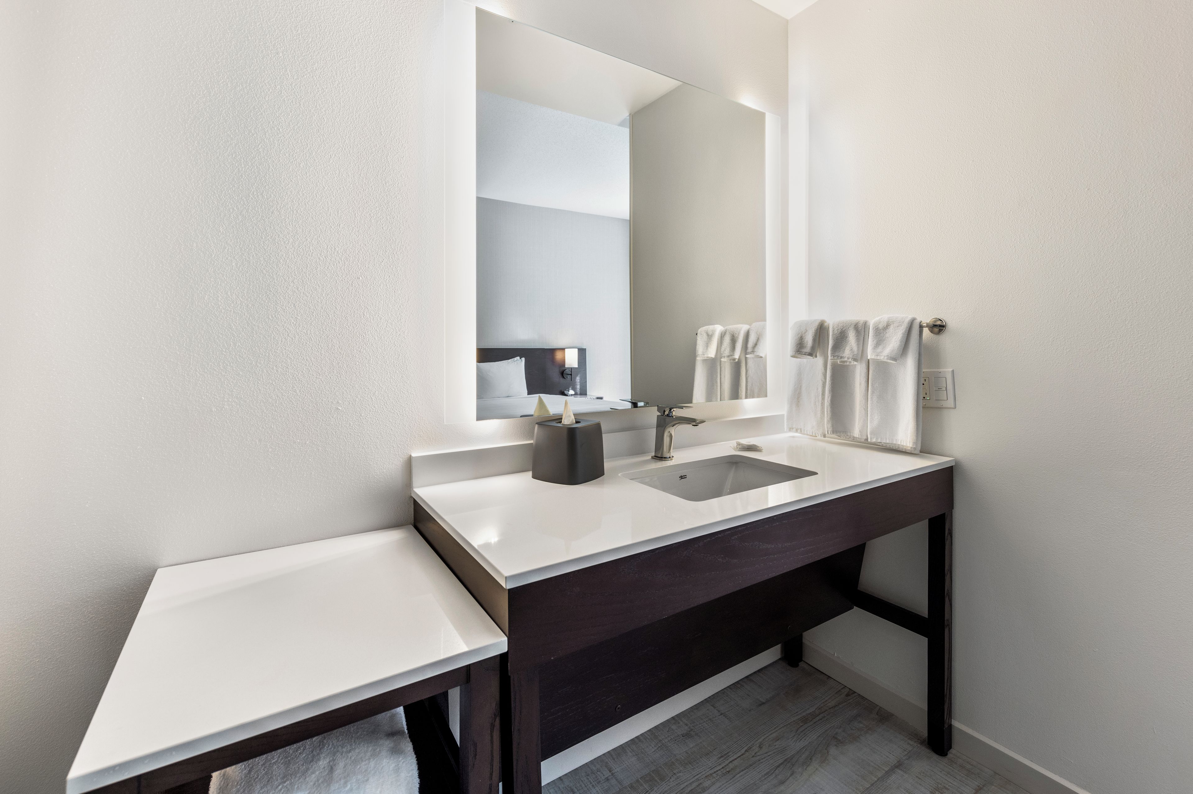 Un baño moderno con tocador blanco, encimera oscura y un espejo grande.