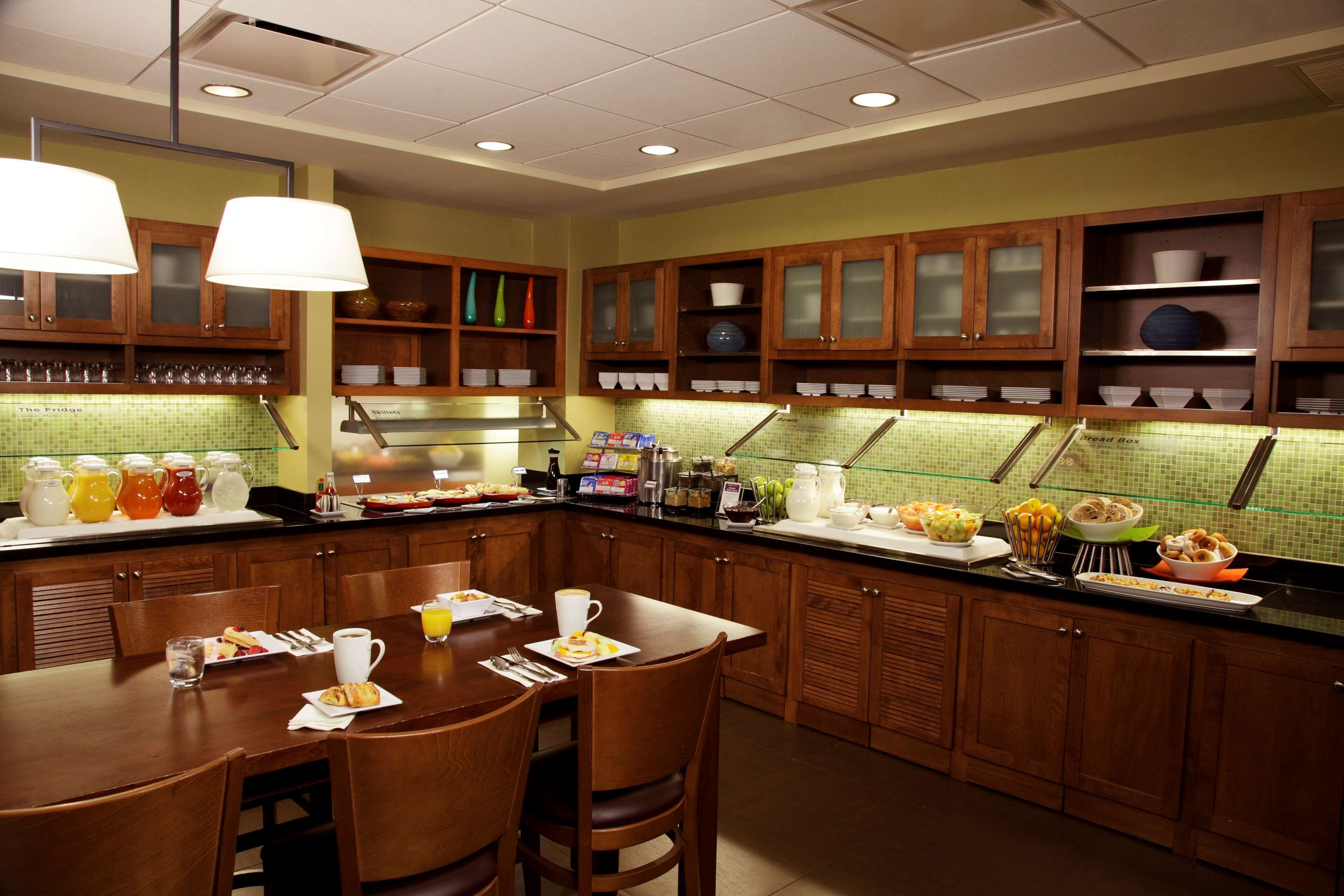 Una cocina de hotel con armarios de madera, una barra de desayuno y diferentes alimentos para el desayuno a la vista.