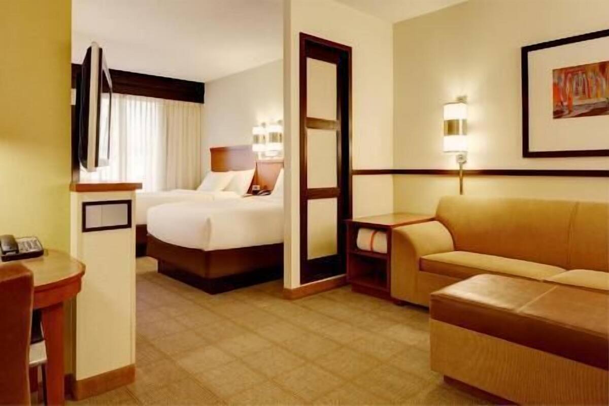 A hotel room with a bed, a sofa, a desk, and a mirror.