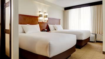 Habitación de hotel con dos camas, cabecero de madera, luces fijadas a la pared y un amplio ventanal con cortinas.